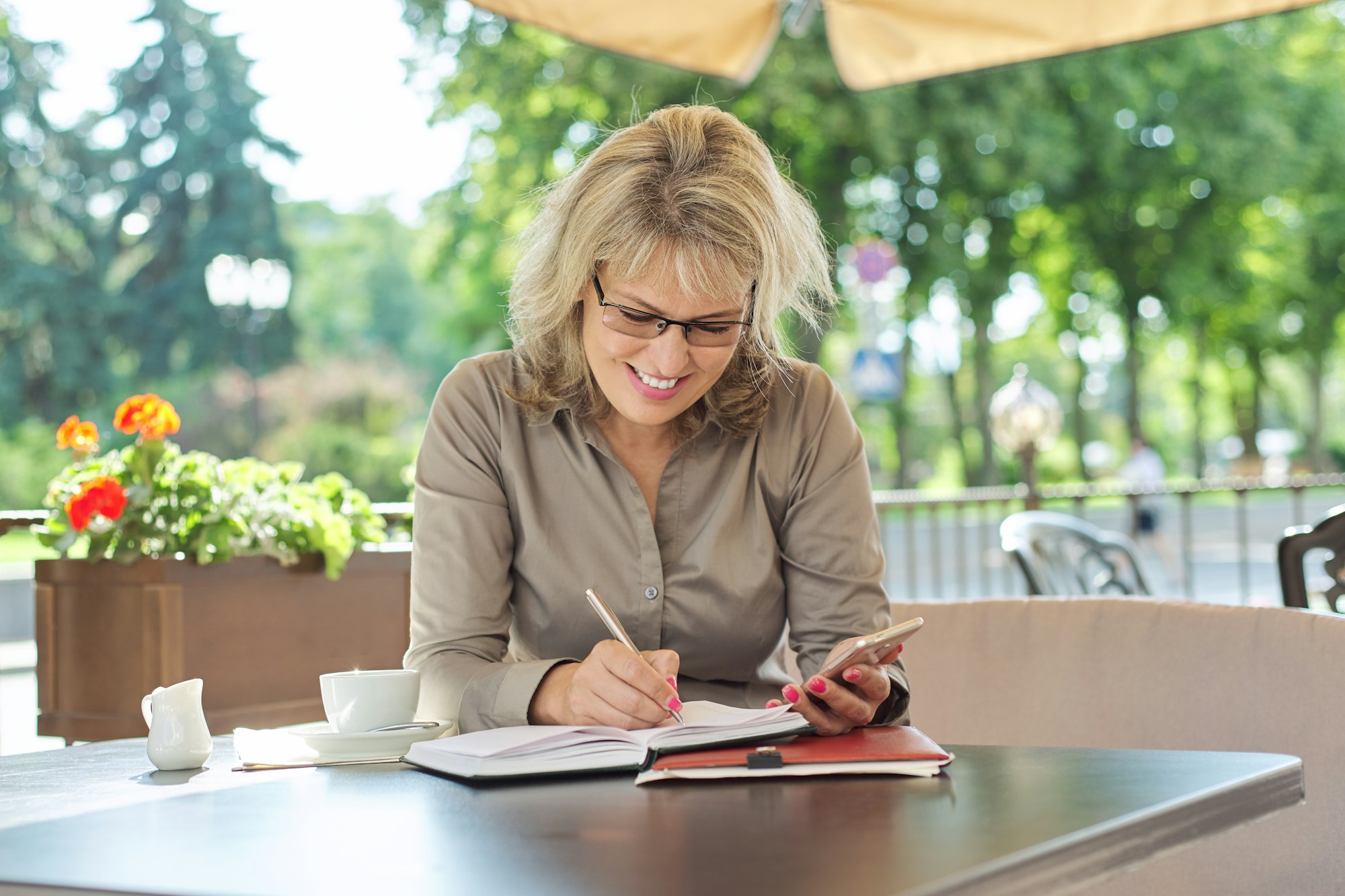 Business beautiful woman writing in business notebook using smartphone